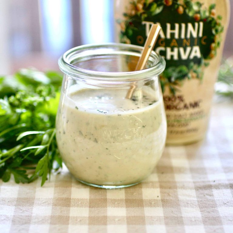 A jar of herby tahini dressing with a spoon in the jar